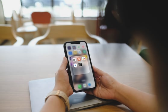 A person holding an iPhone with a folder of popular AI tools, including ChatGPT, Gemini, Claude, and Midjourney.