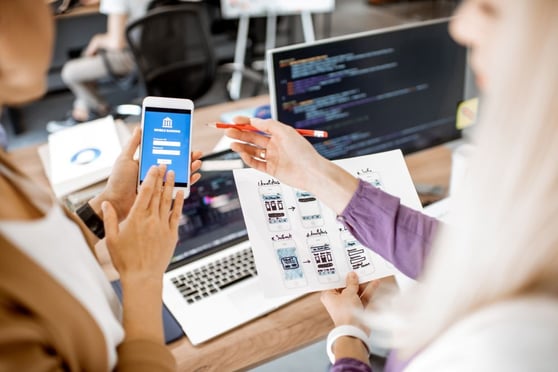 Designers reviewing mobile app interface with code and wireframes for AI-driven user experience.