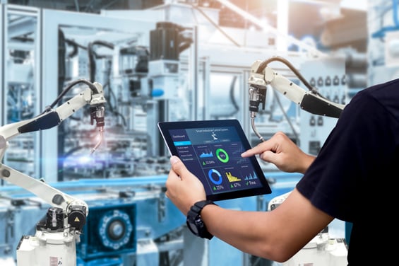 Worker holding a tablet with performance dashboards beside industrial robots, showing AI monitoring in production.