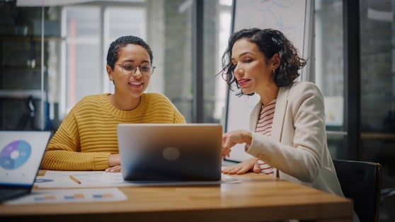 Creative Director and Project Manager Compare Business Results on Laptop.