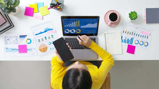 Business owner looking at reports and SEO analysis on her desk with a laptop and a phone