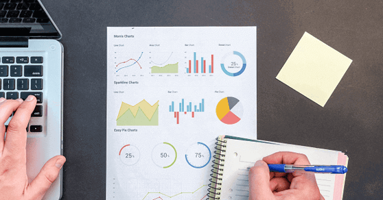 Person writing on a notepad, with an nanalytics report in the background.