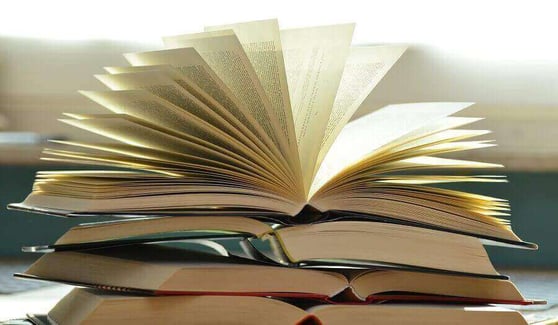 Three books stacked on a table, with the book on top fanned open.