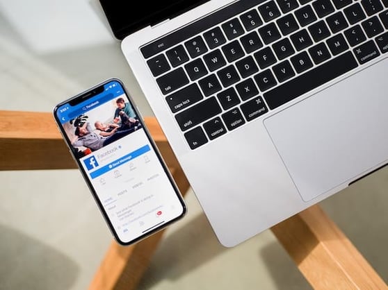 Laptop on a glass-top table, with a cell phone that's open to the Facebook home page.